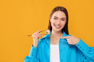 Photo of Happy beautiful young woman holding sushi roll with chopsticks on orange background. Space for text
