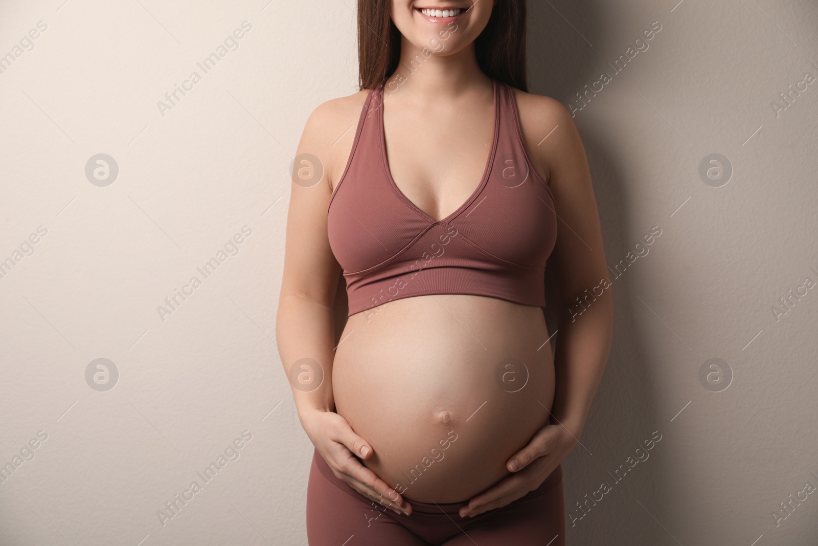 Photo of Pregnant young woman touching belly on beige background, closeup