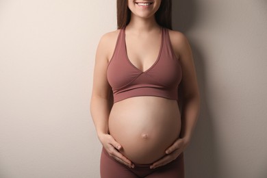 Pregnant young woman touching belly on beige background, closeup