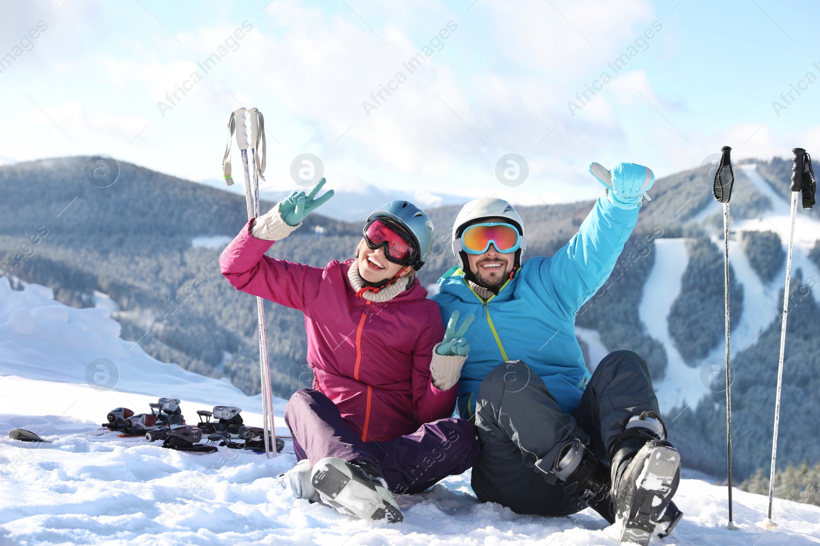 Photo of Happy couple with ski equipment sitting on snowy hill in mountains. Winter vacation