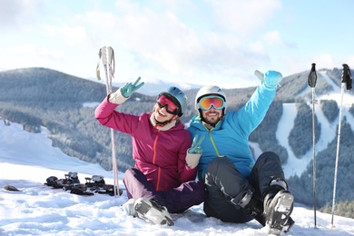 Happy couple with ski equipment sitting on snowy hill in mountains. Winter vacation