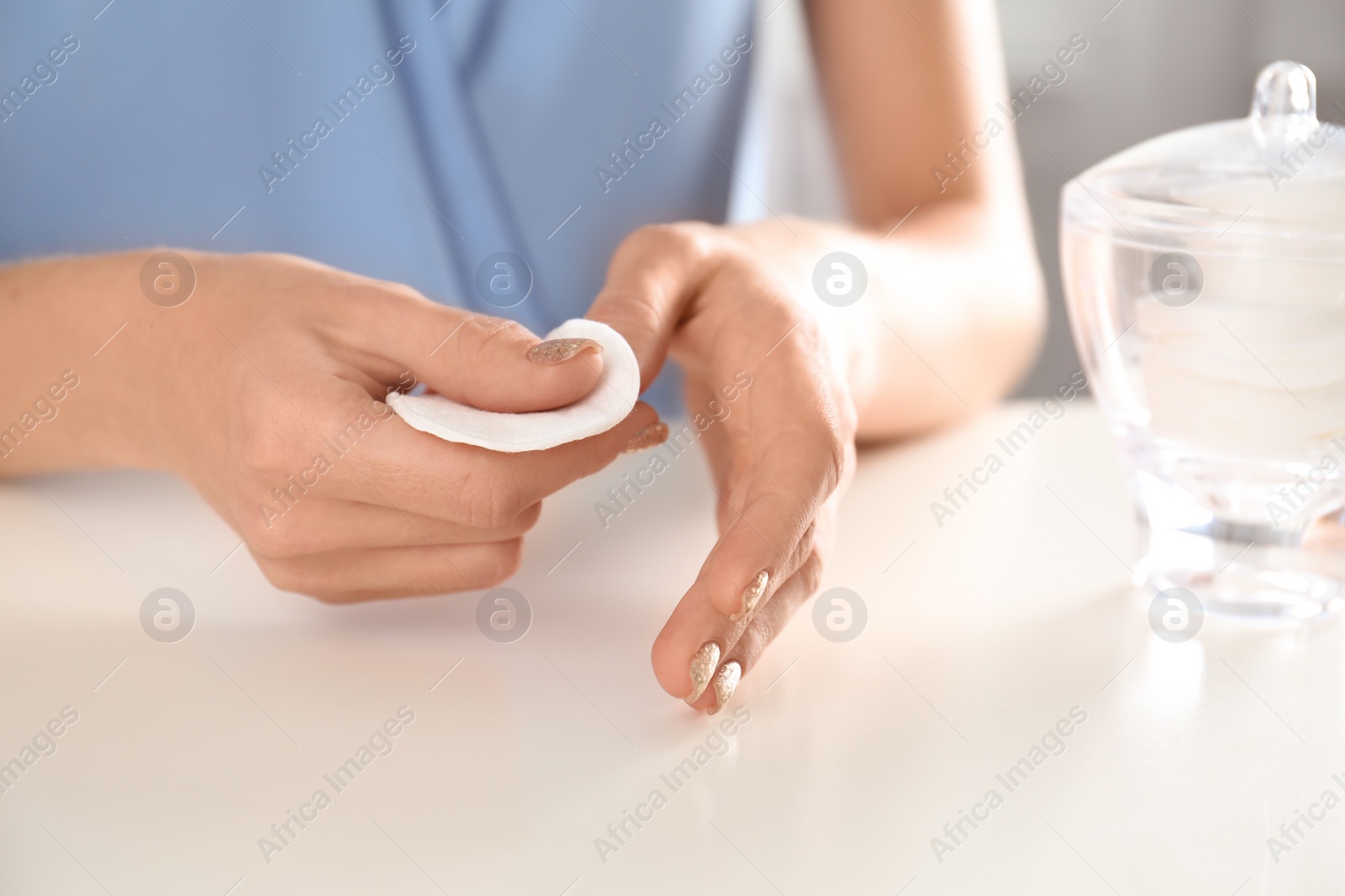 Photo of Woman removing polish from nails with cotton pad at table, closeup