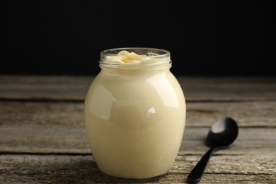 Photo of Jar of delicious mayonnaise and spoon on wooden table