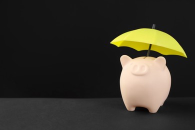 Photo of Small umbrella and piggy bank on black background. Space for text