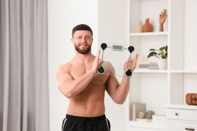 Photo of Portrait of happy athletic man with scales at home. Weight loss concept