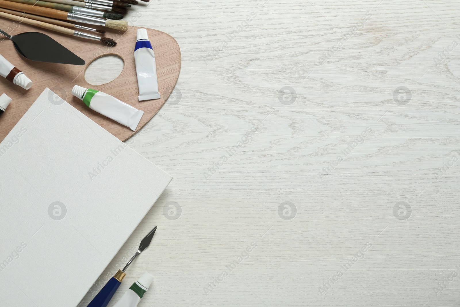 Photo of Blank canvas, tools, palette and paints on white wooden table, flat lay. Space for text