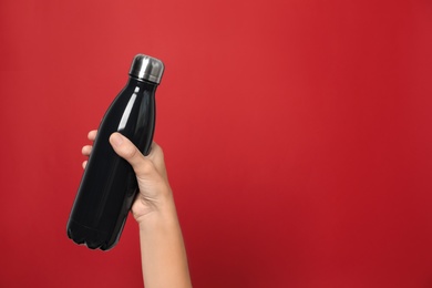 Woman holding modern dark  thermos on red background, closeup. Space for text