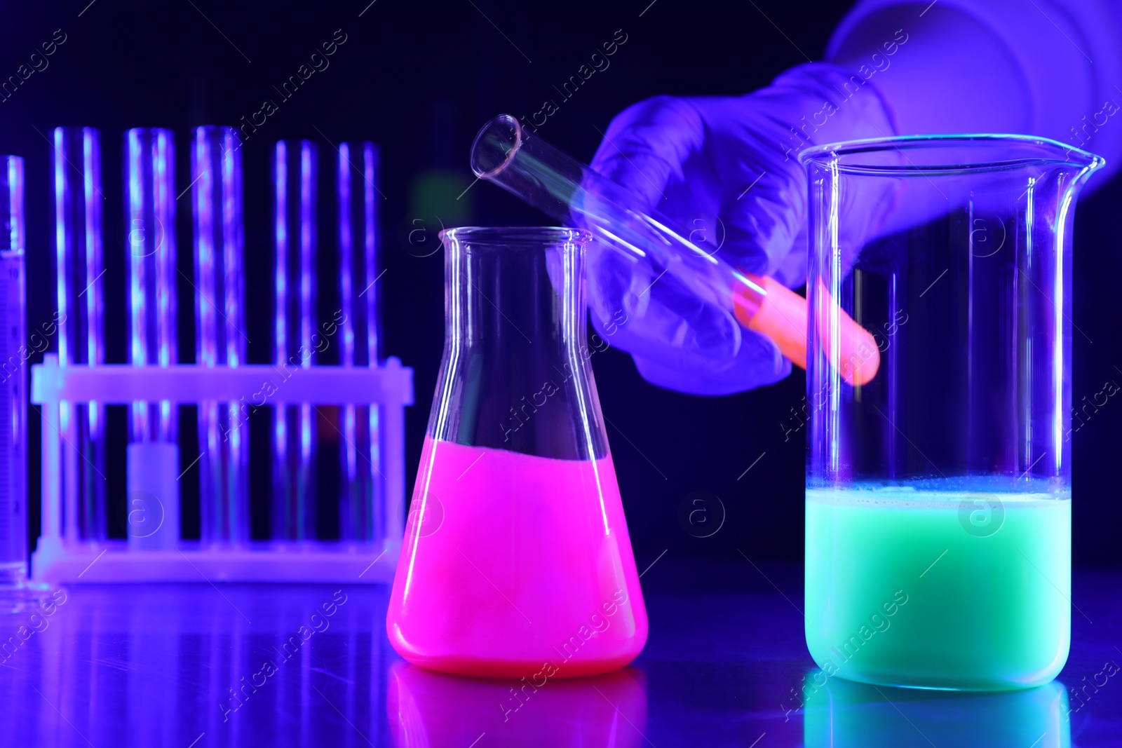 Photo of Scientist pouring luminous liquid into laboratory glassware at table, selective focus