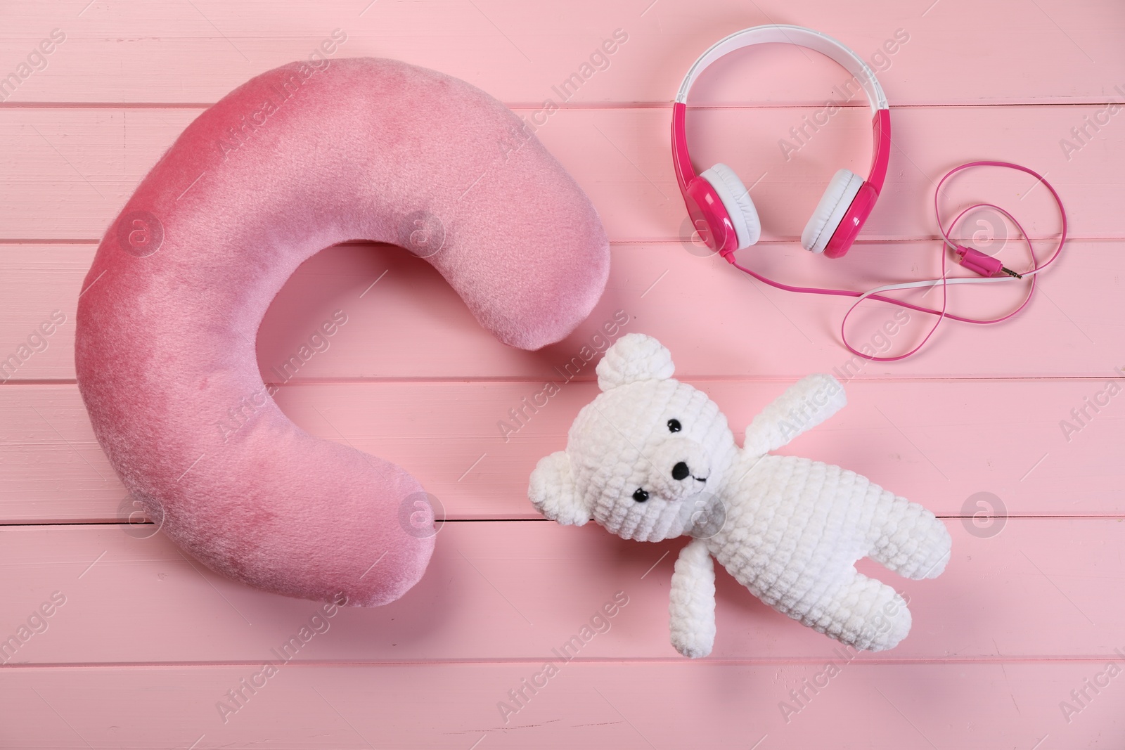 Photo of Travel pillow, toy bear and headphones on pink wooden background, flat lay