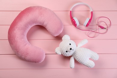 Photo of Travel pillow, toy bear and headphones on pink wooden background, flat lay