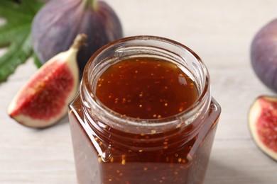 Jar of tasty sweet jam and fresh figs on white table, closeup