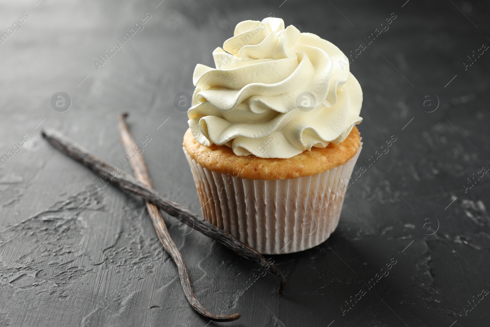 Photo of Tasty cupcake with cream and vanilla pods on black table, closeup