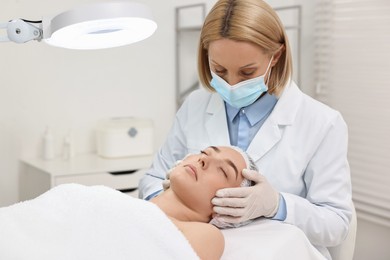 Dermatologist examining patient`s face under lamp in clinic