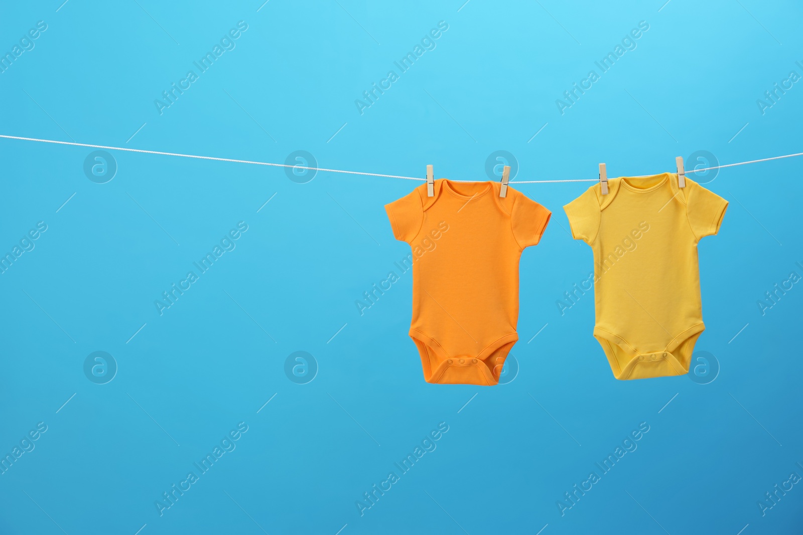 Photo of Colorful baby onesies hanging on clothes line against blue background, space for text. Laundry day