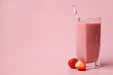 Glass with delicious berry smoothie and fresh strawberries on pink background. Space for text