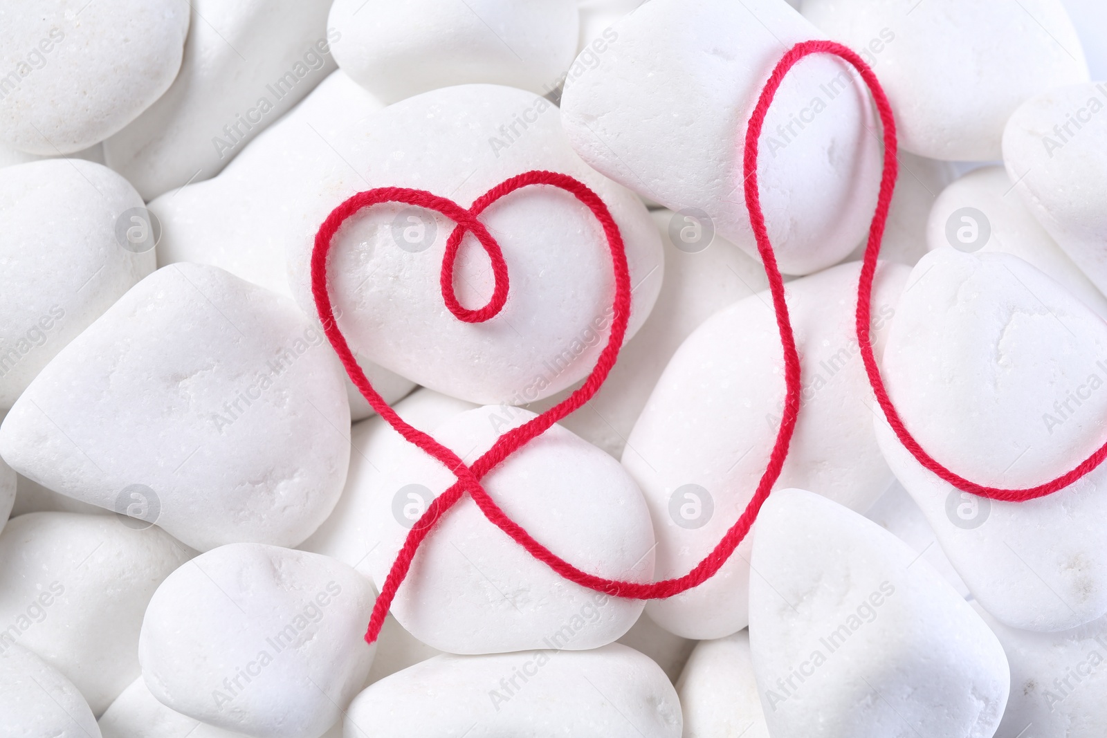 Photo of Heart made of thread on white pebble stones, top view