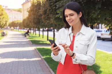 Photo of Beautiful young woman with smartphone on walkway outdoors, space for text
