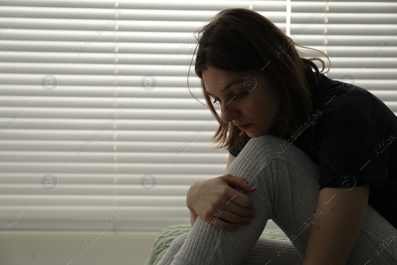 Photo of Sad young woman near window indoors, space for text