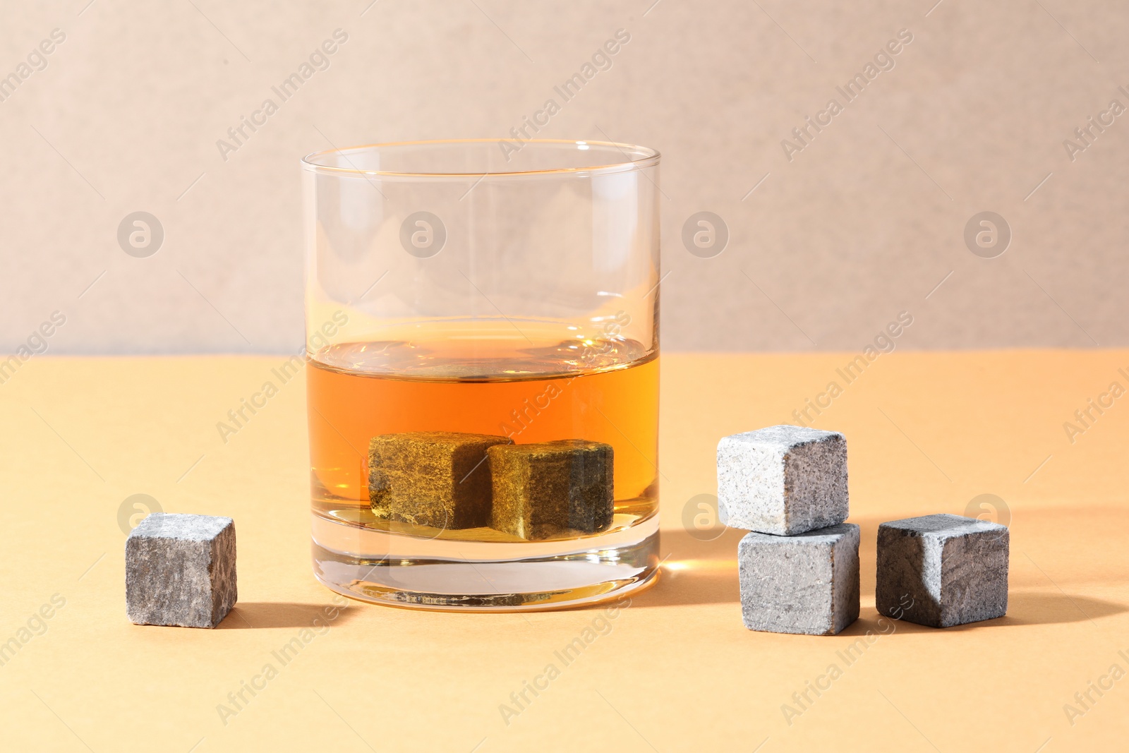 Photo of Whiskey stones and drink in glass on orange table, closeup