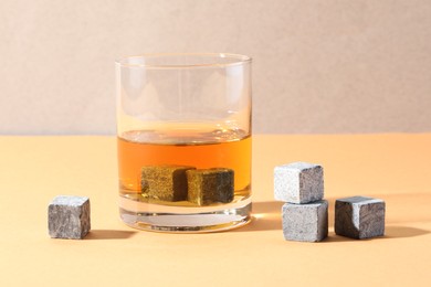 Whiskey stones and drink in glass on orange table, closeup