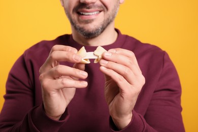 Happy man holding tasty fortune cookie with prediction on orange background, closeup