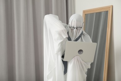 Overworked ghost. Man in white sheet using laptop at home