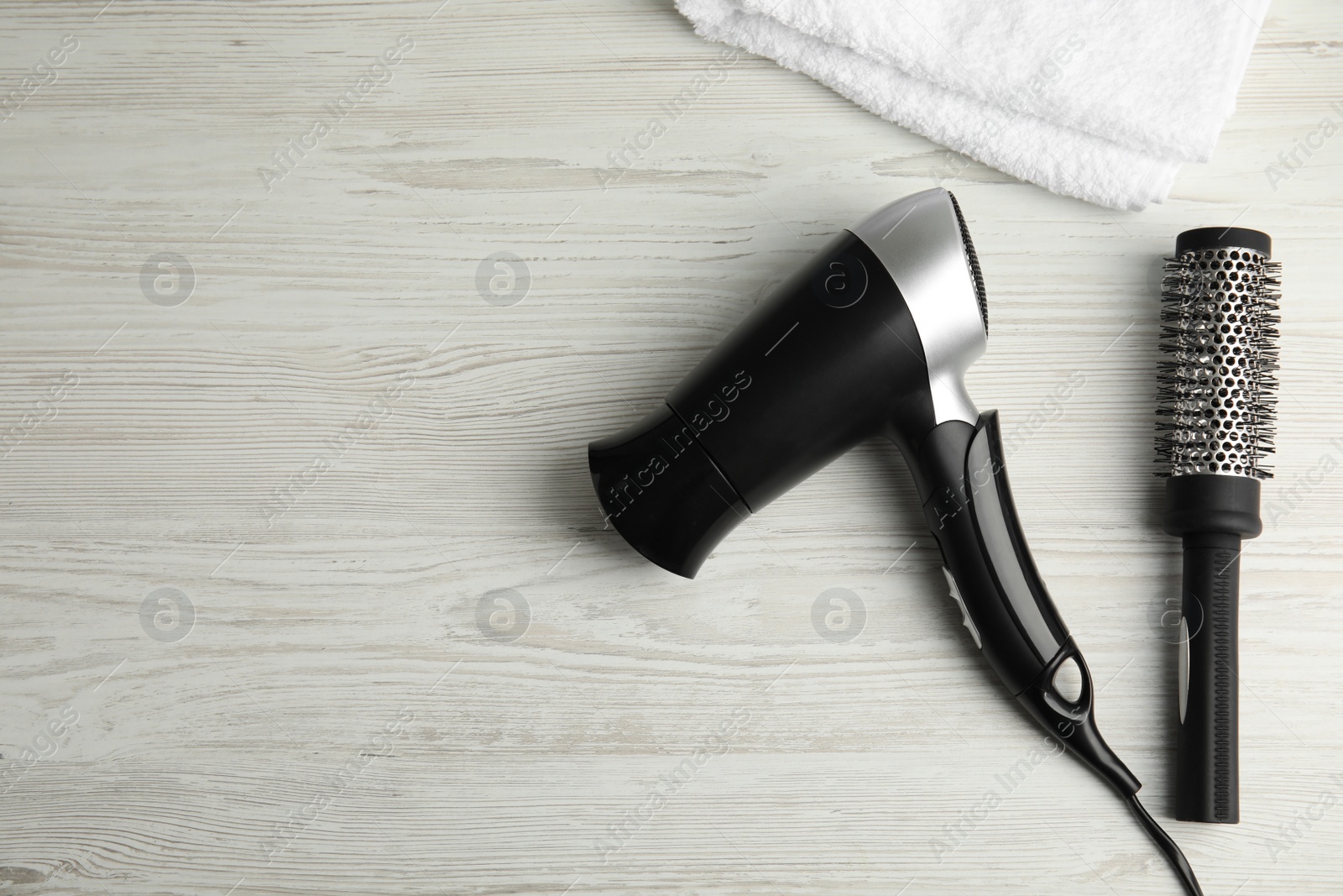 Photo of Modern hair dryer, towel and round brush on white wooden table, flat lay. Space for text