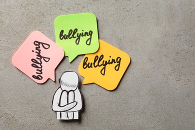 Photo of Child paper figure and stickers with word Bullying on light stone surface, flat lay. Space for text