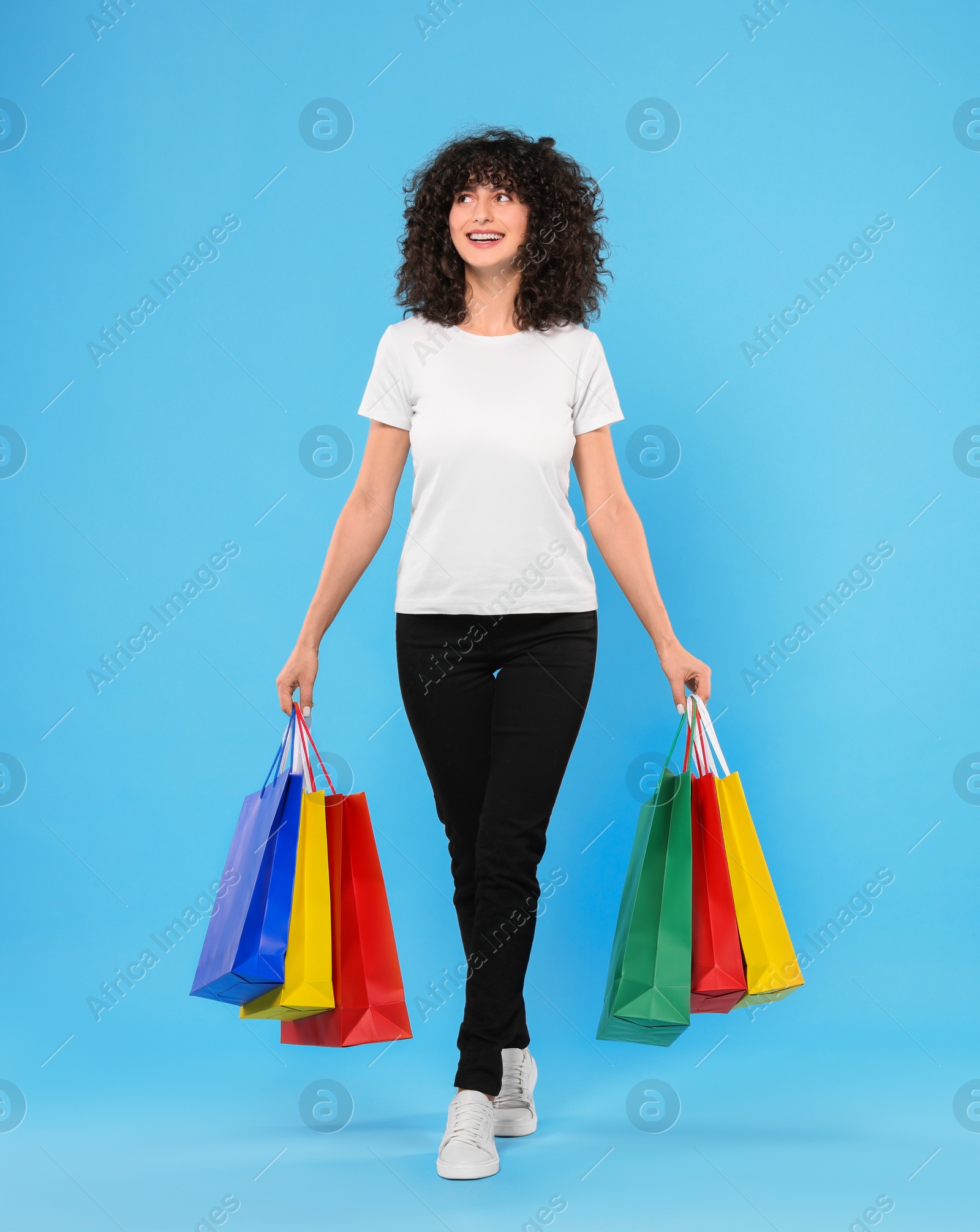 Photo of Happy young woman with shopping bags on light blue background