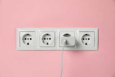 Photo of Charger adapter plugged into power sockets on pink wall. Electrical supply