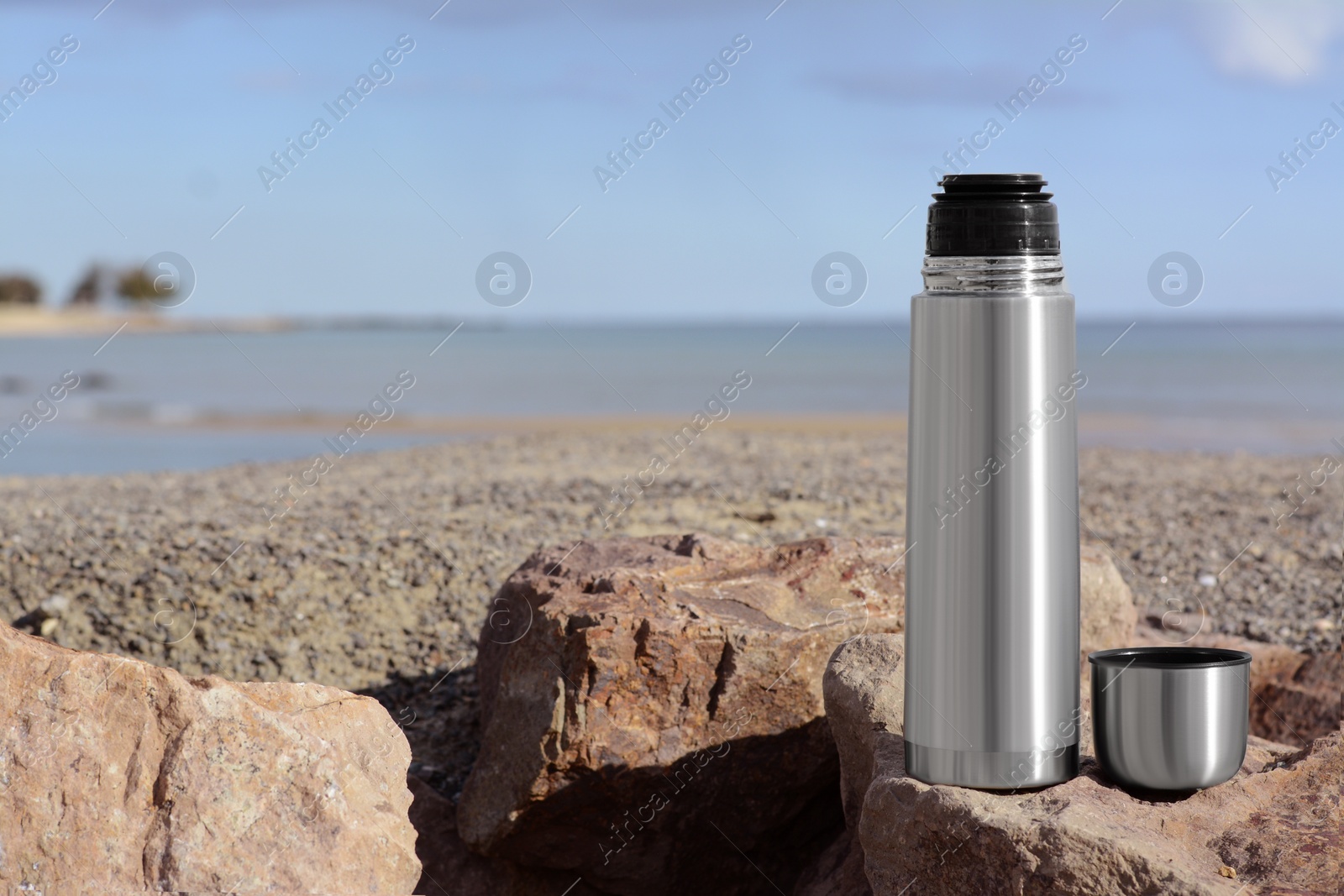 Photo of Metallic thermos and cap on stone near sea, space for text