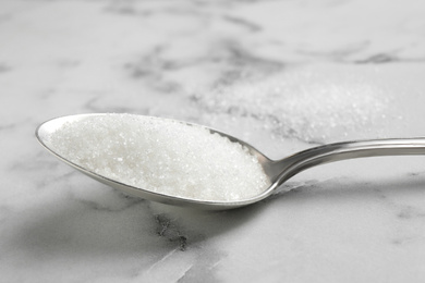 Spoon of white sugar on marble table, closeup