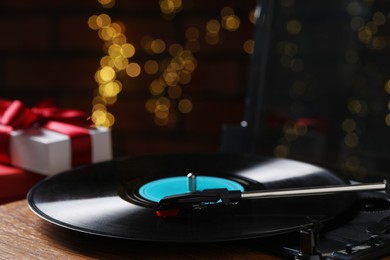 Turntable with vinyl record and Christmas gift boxes against blurred lights, closeup