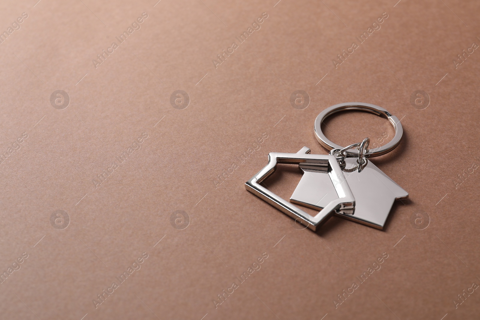 Photo of Metallic keychains in shape of houses on light brown background. Space for text
