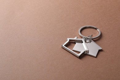 Photo of Metallic keychains in shape of houses on light brown background. Space for text