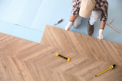 Photo of Worker installing laminated wooden floor indoors, above view