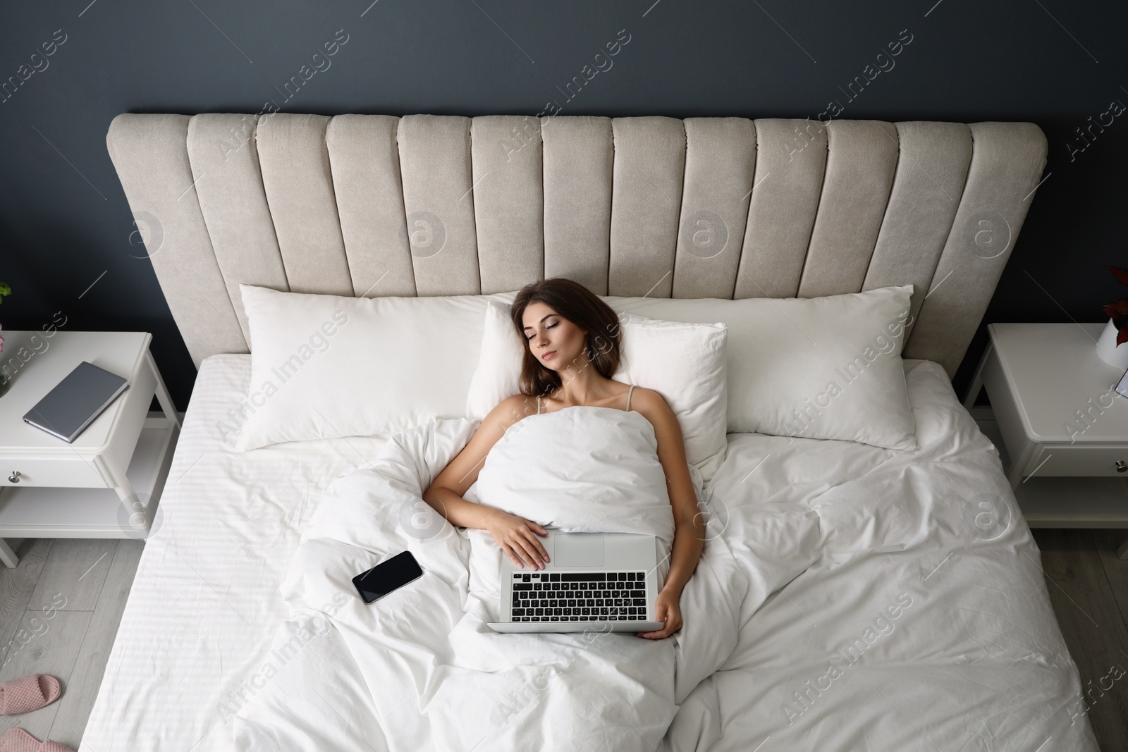 Photo of Tired woman with laptop and smartphone sleeping in bed at home, above view