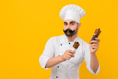 Photo of Professional chef with funny artificial moustache holding shakers on yellow background. Space for text