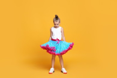 Photo of Cute little girl in tutu skirt dancing on yellow background