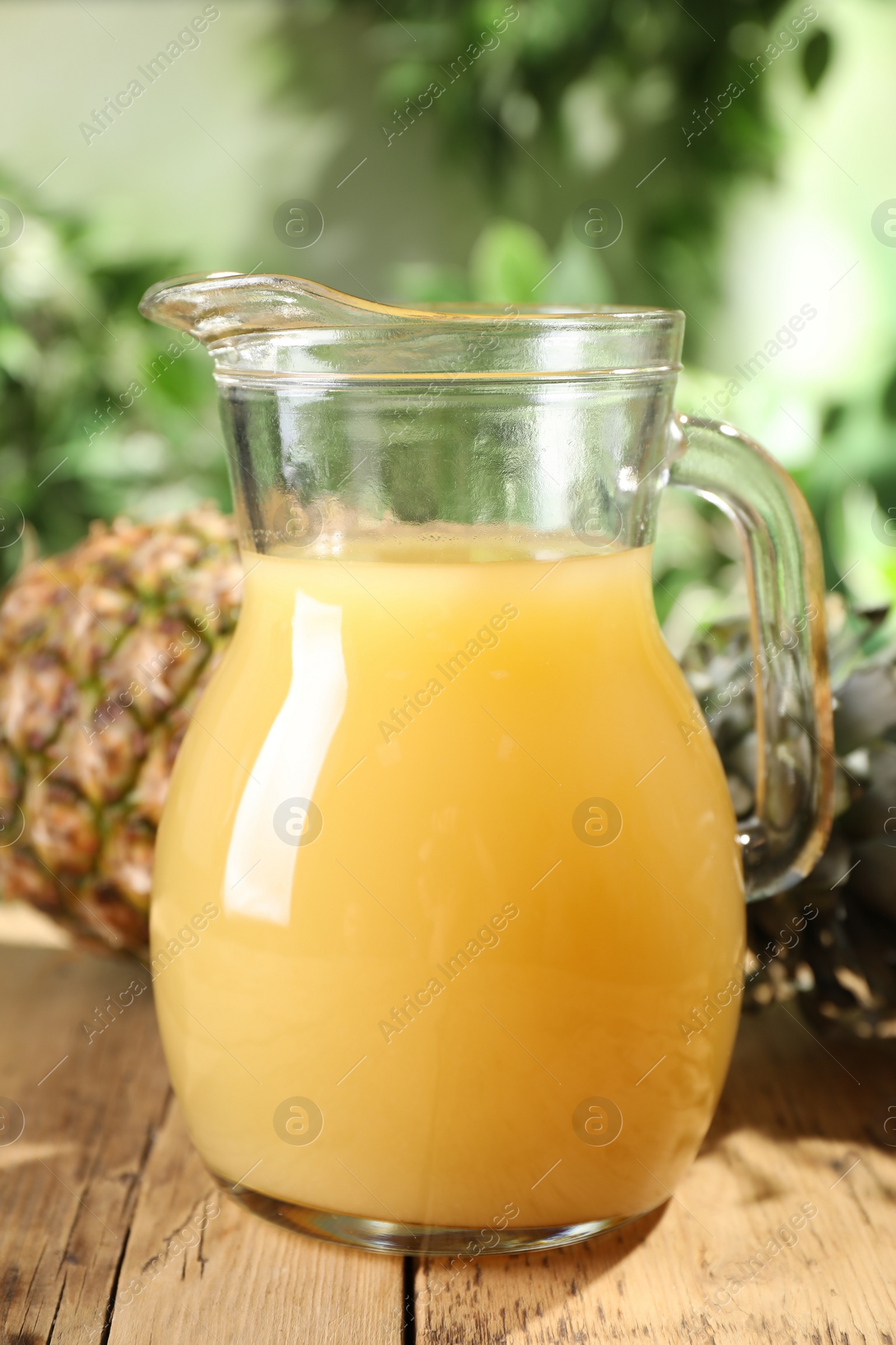 Photo of Delicious pineapple juice and fresh fruit on wooden table against blurred background