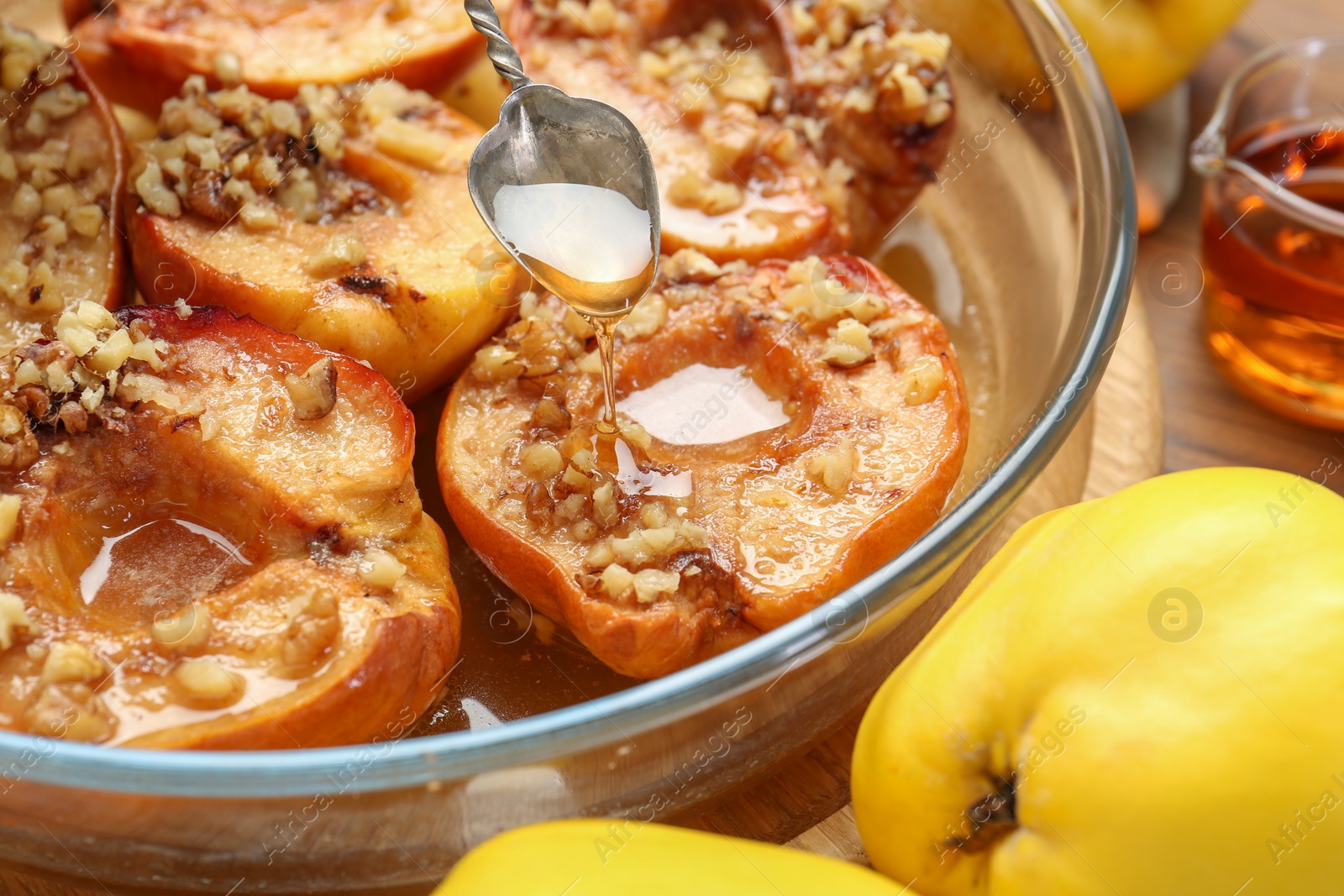 Photo of Pouring tasty honey onto baked quinces in bowl on table, closeup