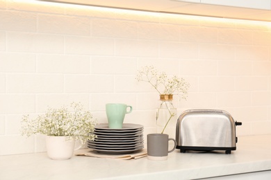Photo of Modern toaster, crockery and flowers on counter in kitchen