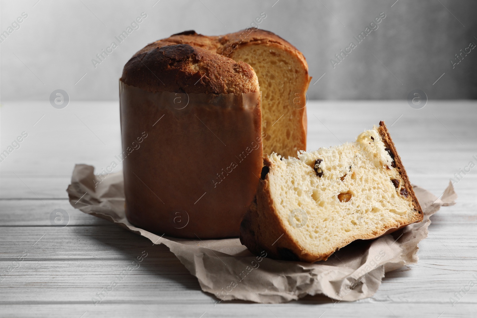 Photo of Delicious cut Panettone cake with raisins on white wooden table. Traditional Italian pastry