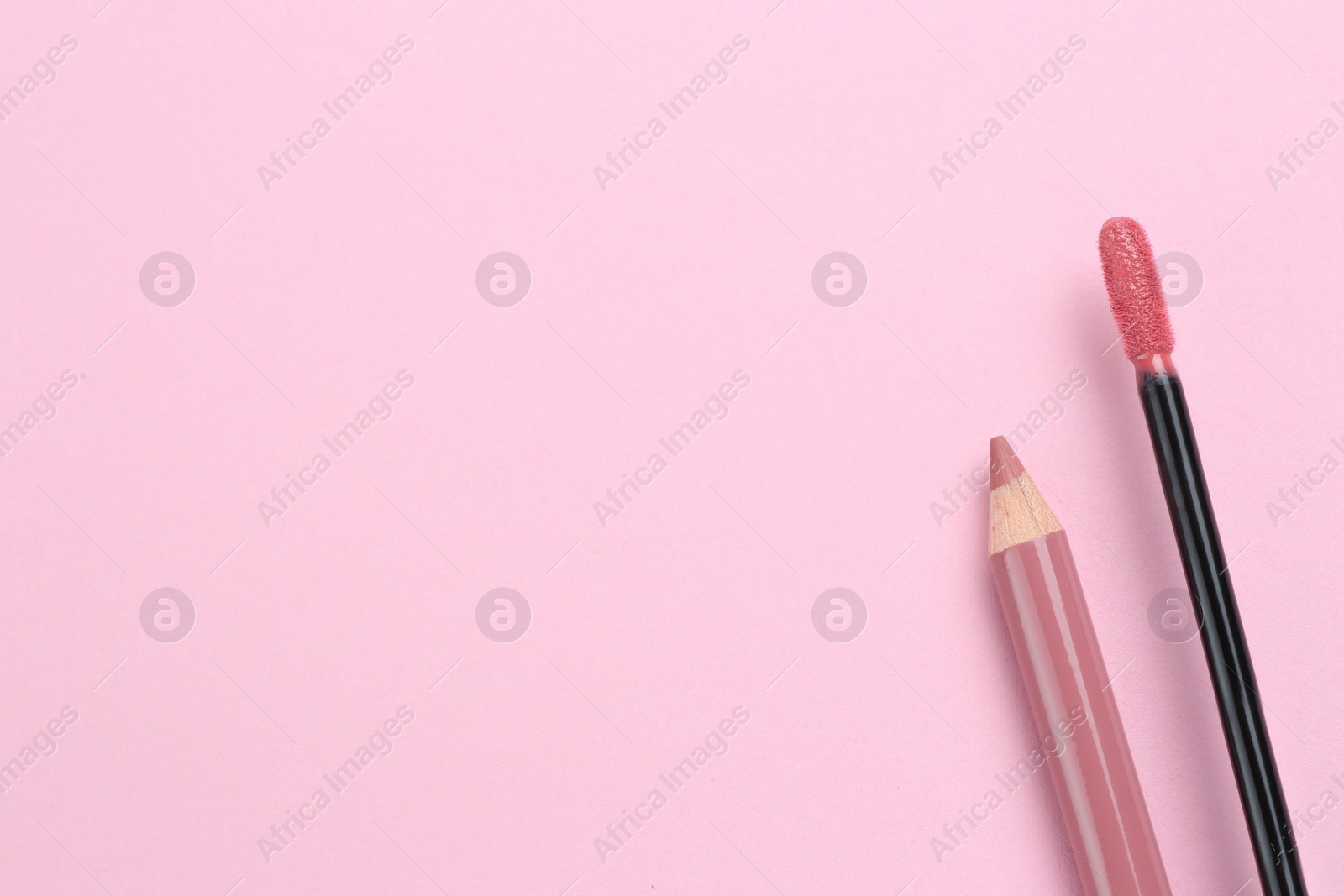 Photo of Bright lip pencil and brush of liquid lipstick on pink background, flat lay with space for text. Cosmetic products