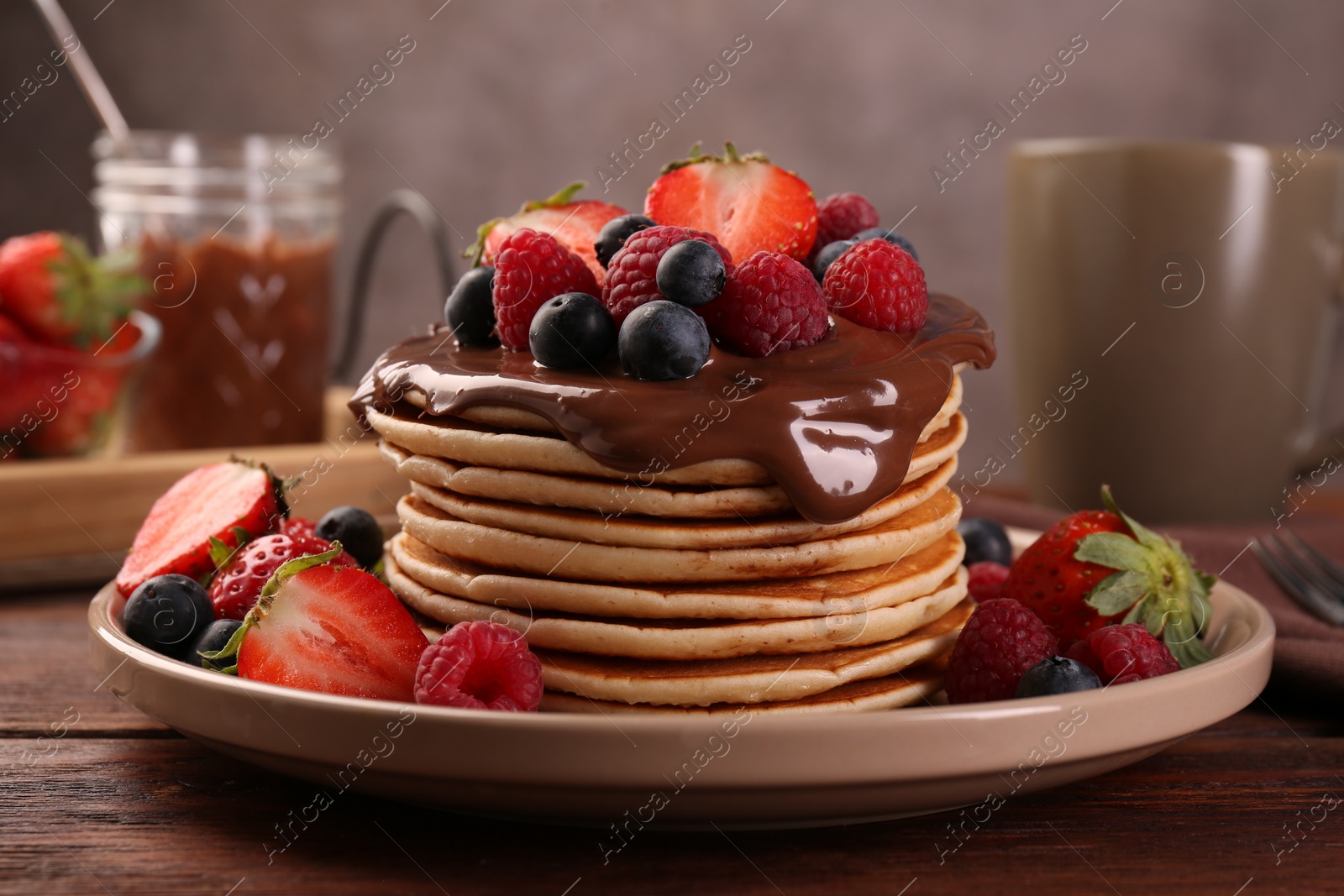 Photo of Stack of tasty pancakes with fresh berries and chocolate spread on wooden table, closeup