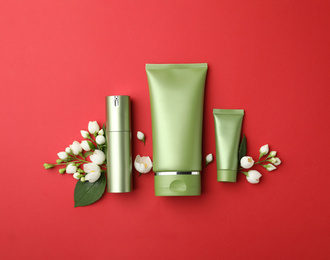 Set of cosmetic products and flowers on red background, flat lay