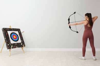 Woman with bow and arrow aiming at archery target indoors, back view