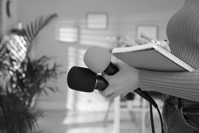 Professional journalist with microphones taking notes indoors, closeup. Black and white effect