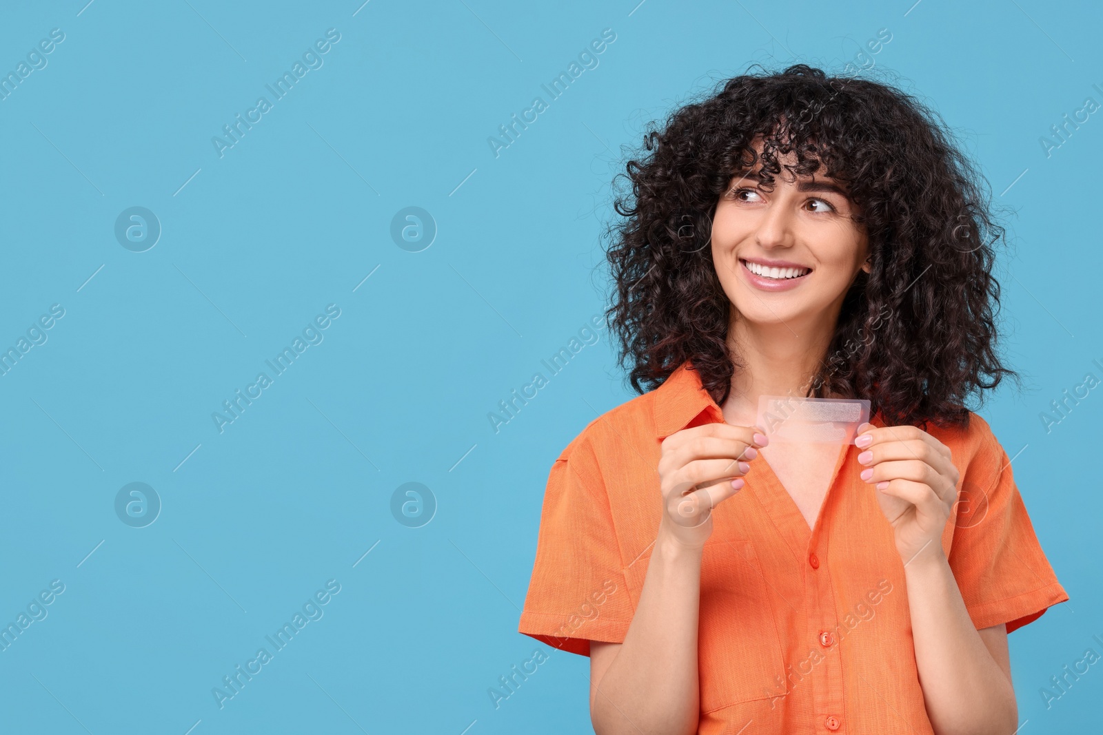 Photo of Young woman holding teeth whitening strips on light blue background, space for text