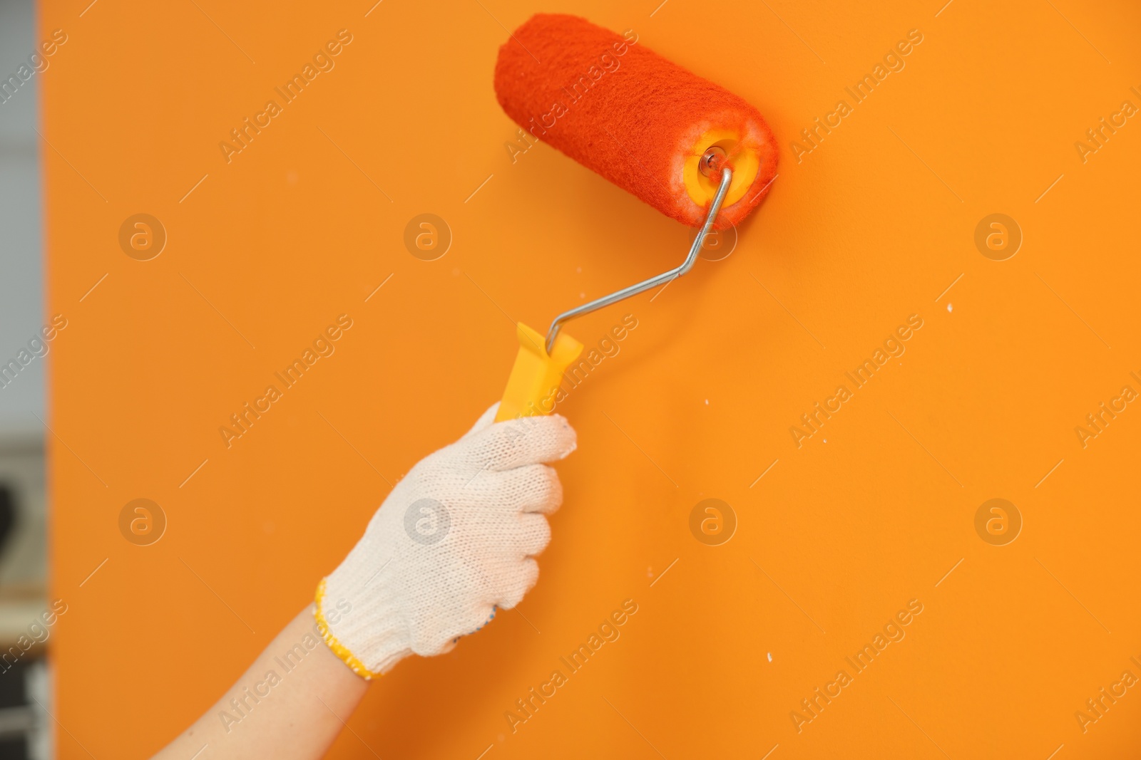 Photo of Designer painting orange wall with roller, closeup